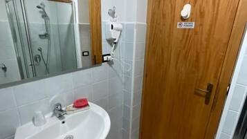 Une salle de bain avec un lavabo blanc, une cabine de douche en verre et une porte en bois avec une pancarte.