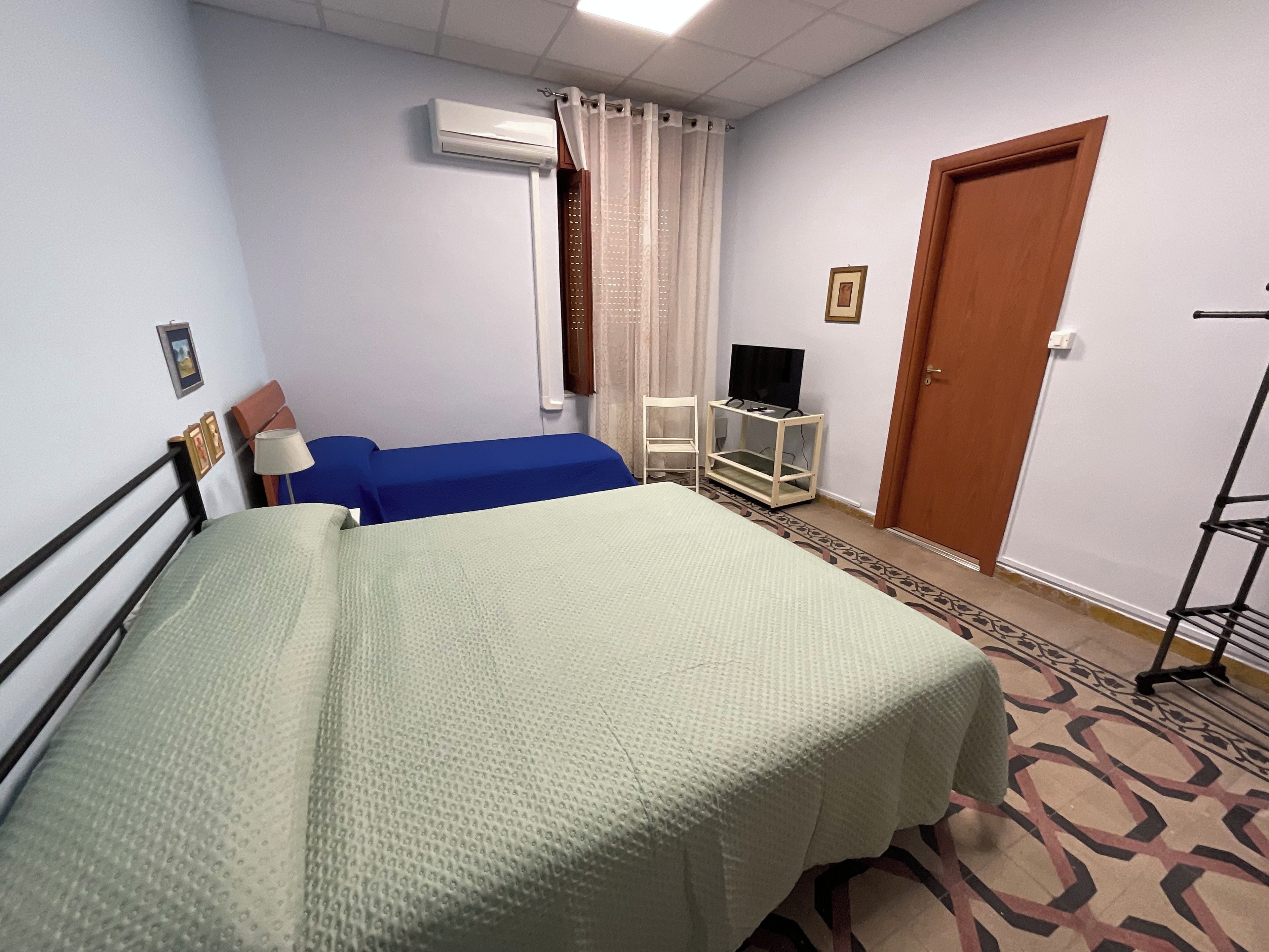 Une chambre d’hôtel avec un lit, un téléviseur posé sur un meuble, un appareil de climatisation, une porte et un tapis à motifs.