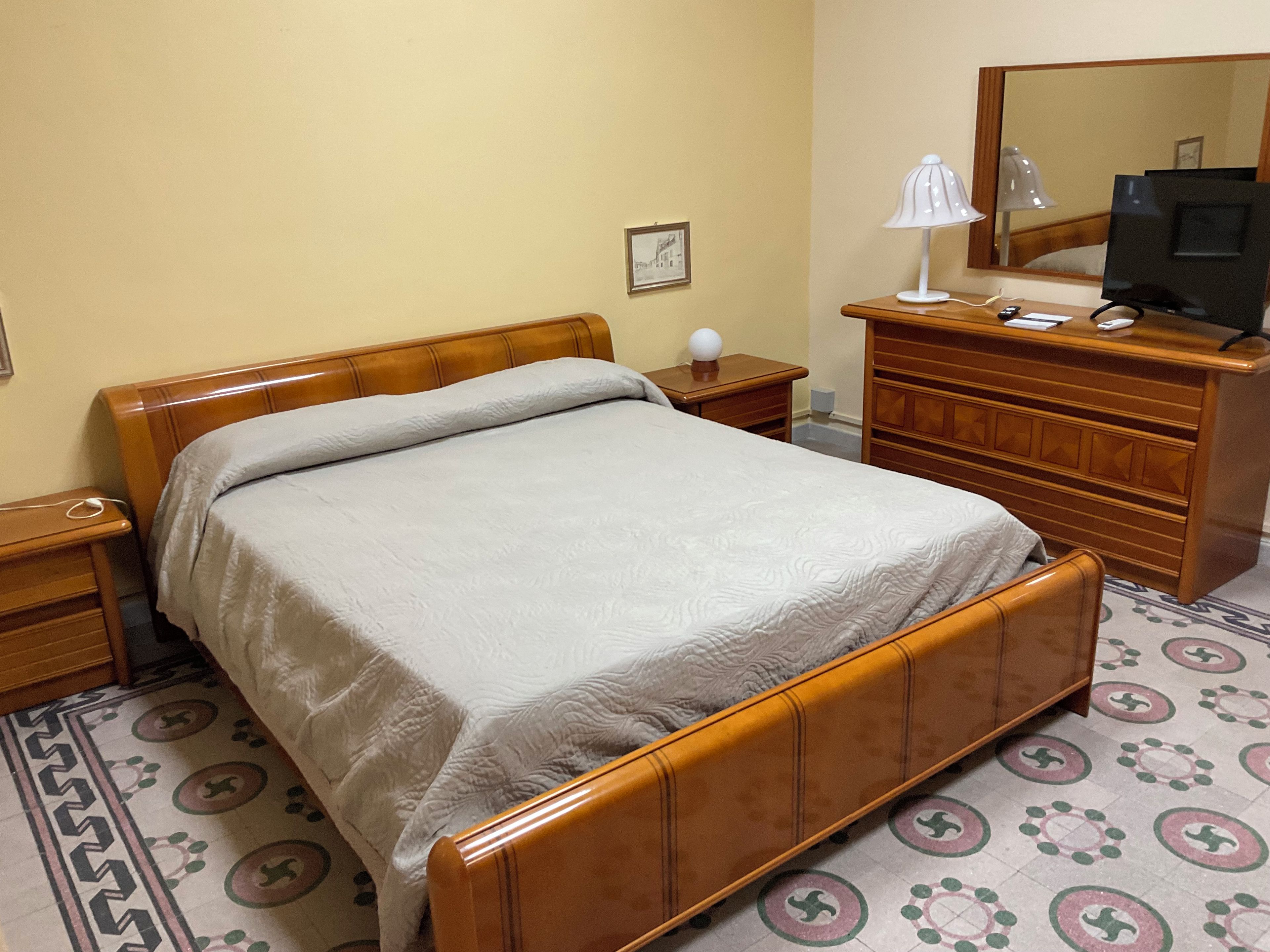 Una habitación de hotel con una cama de madera, un aparador, un escritorio, una lámpara y un televisor.