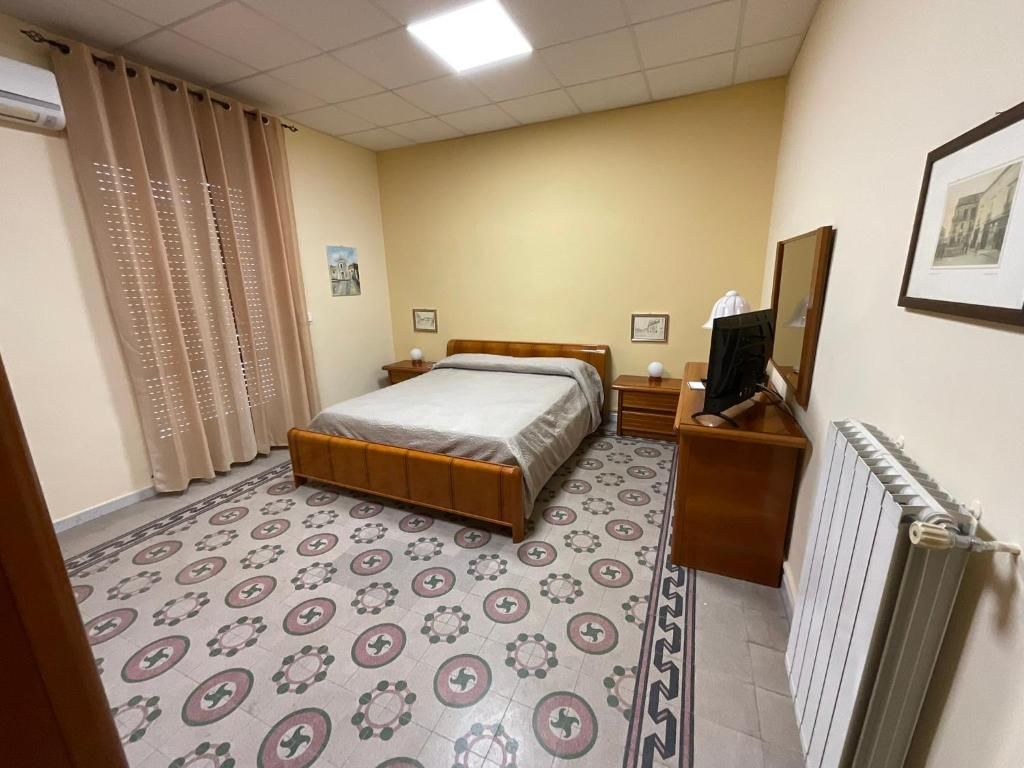 A hotel room with a bed, bedside tables, a TV, a radiator, and patterned floor tiles.
