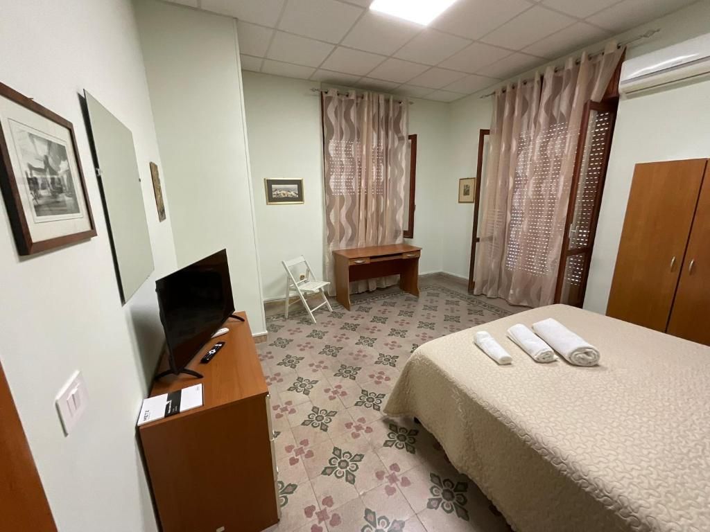 Quarto de hotel com cama, escrivaninha, computador, cadeira e cortinas.