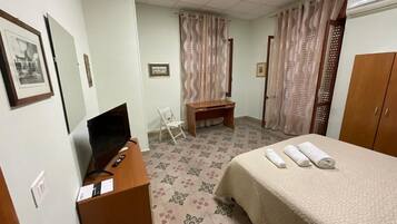 Quarto de hotel com cama, escrivaninha, computador, cadeira e cortinas.