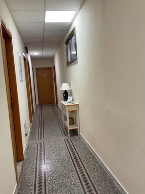 Un pasillo de hotel con piso alfombrado, un escritorio con lámpara y una puerta al fondo.