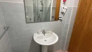 Ein Badezimmer mit einem Standwaschbecken, einem Spiegel darüber, einer Duschkabine und einer Holztür.