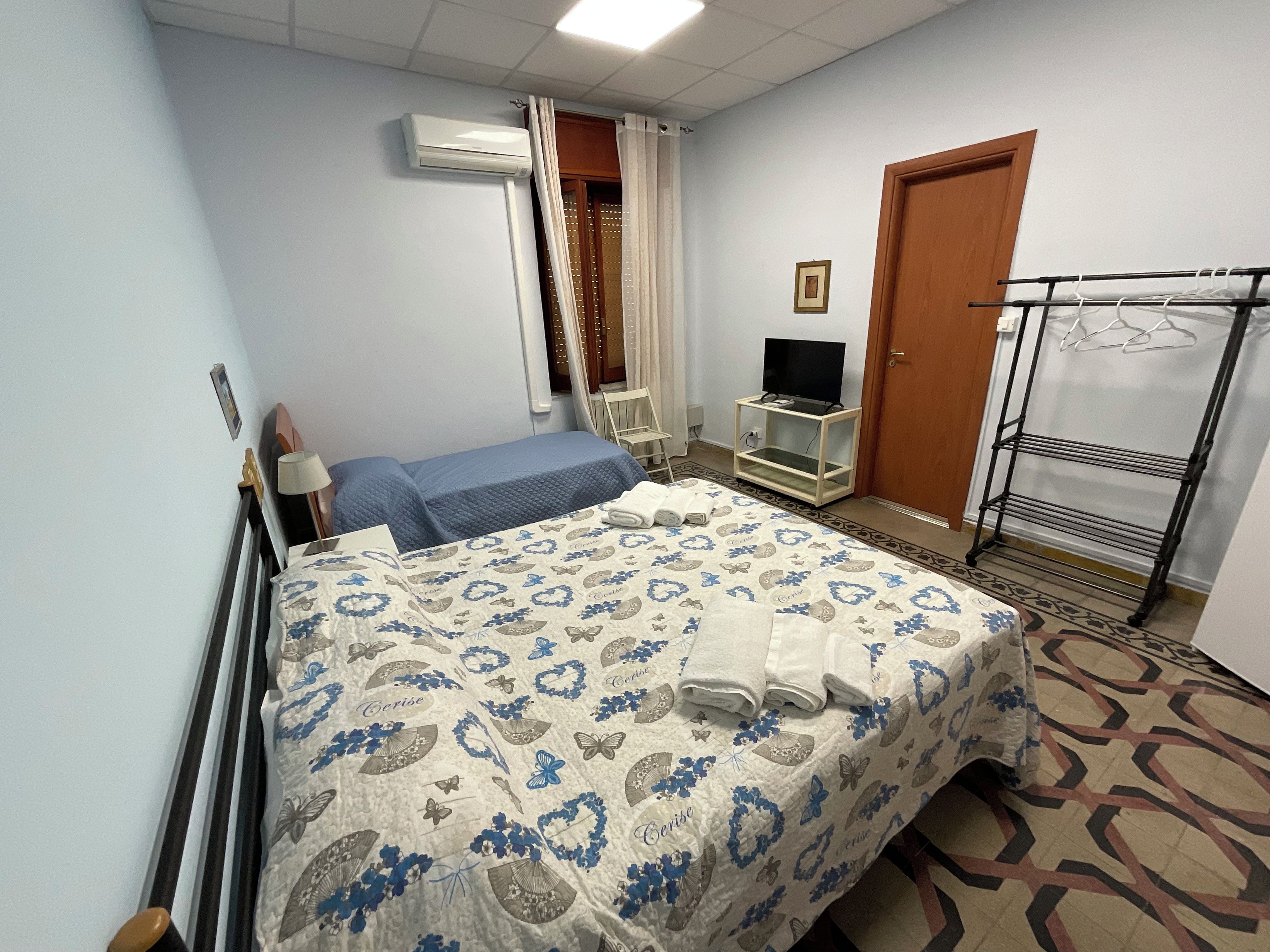 Ein Hotelzimmer mit einem Bett, einem Fernseher auf einem Tisch, einem Kleiderständer und einer Klimaanlage.