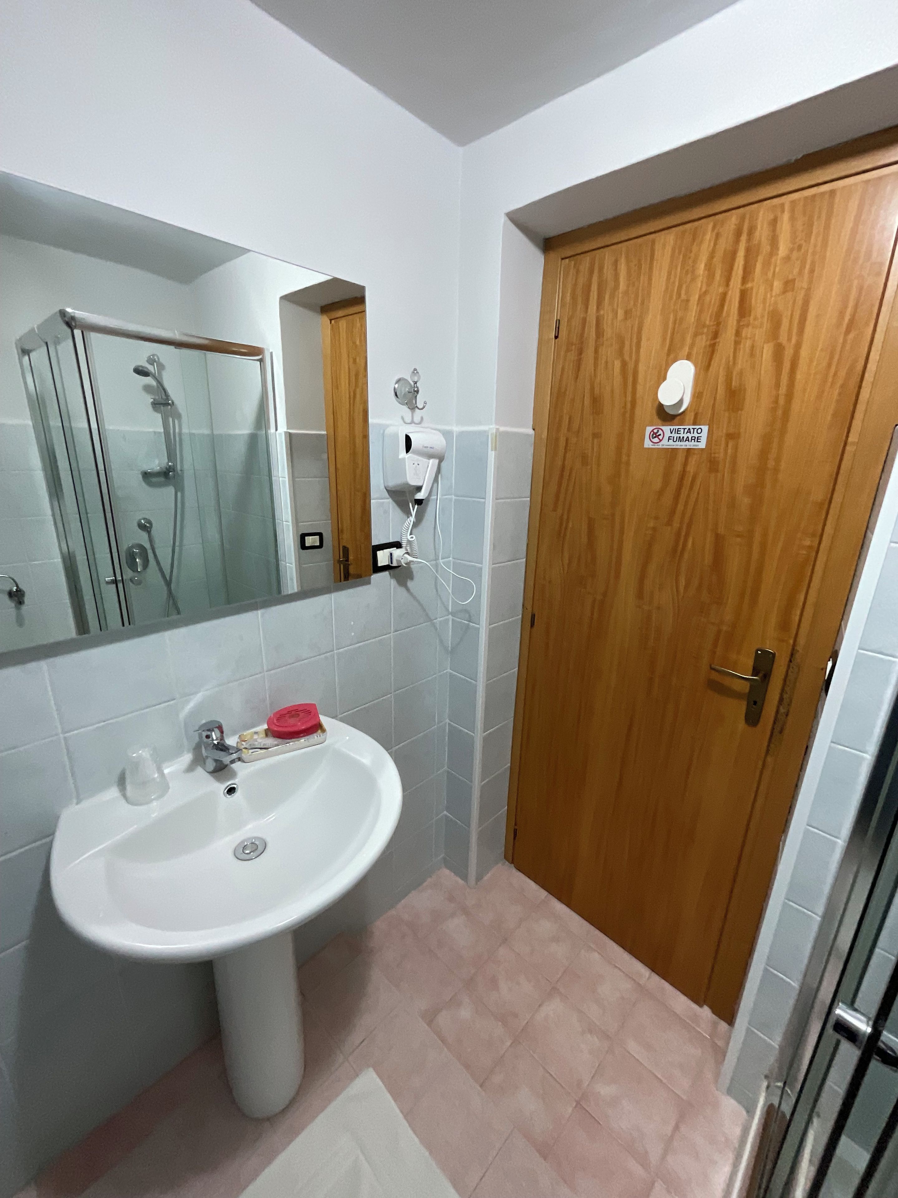 Une salle de bain avec un lavabo blanc, une cabine de douche en verre et une porte en bois ornée d’un autocollant.