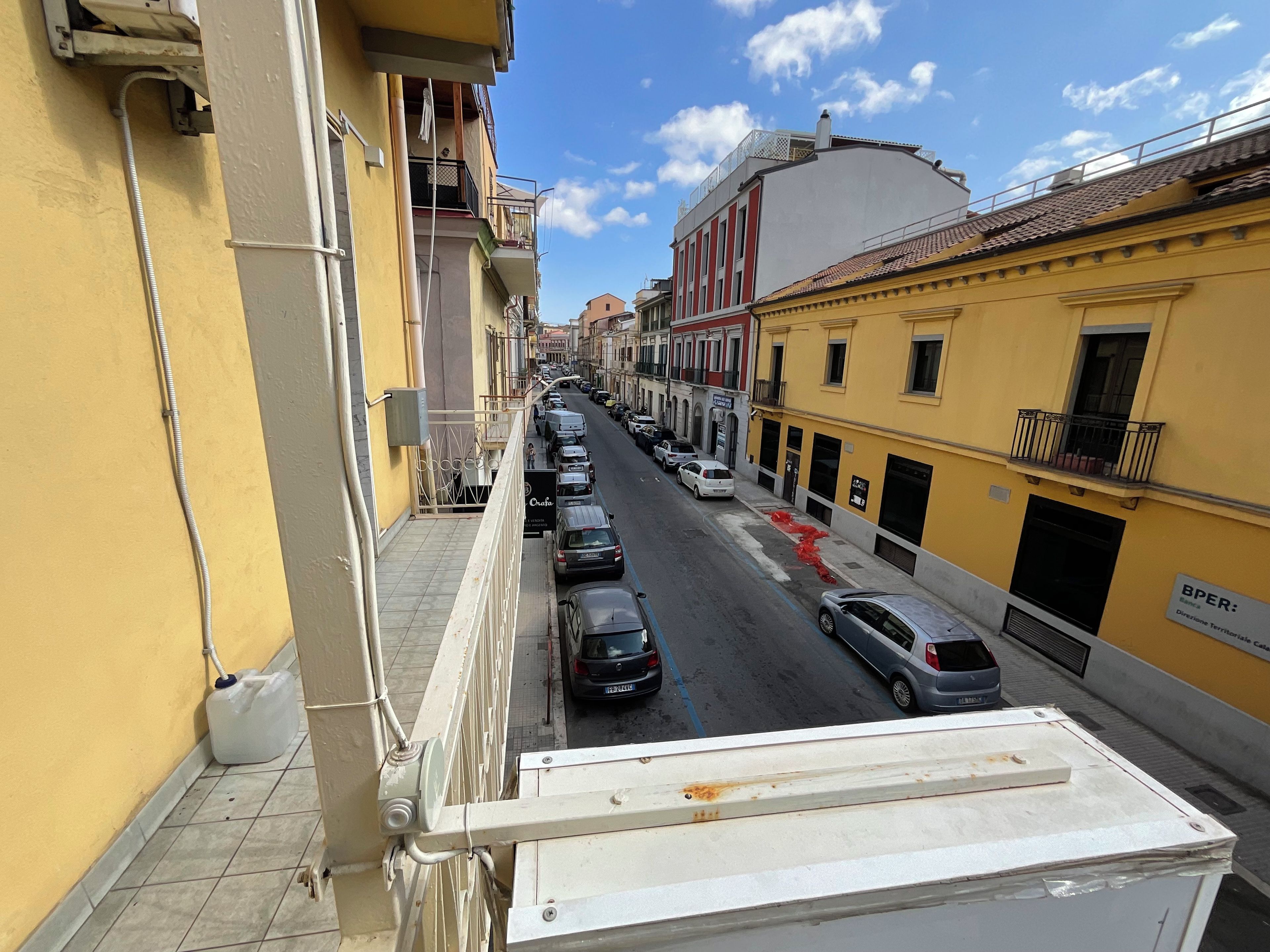Une rue étroite, bordée de voitures garées et d’immeubles des deux côtés.