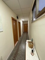 Un pasillo con puertas de madera, suelo de baldosas con un borde decorativo y una ventana a la derecha.