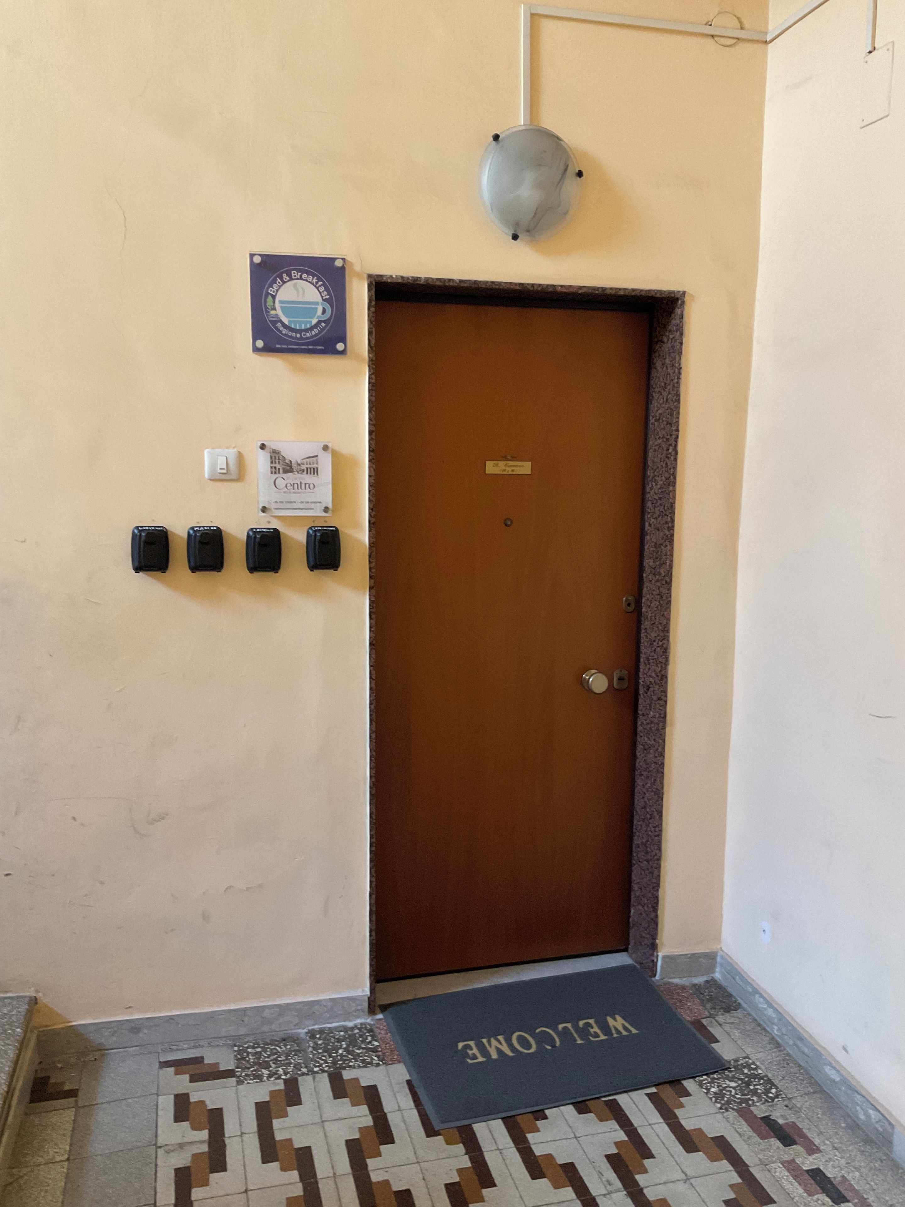 Een hotel ingang met een houten deur, een welkomstmat, een lichtschakelaar en een bord dat het centrum van het hotel aangeeft.