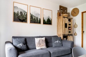 A living room with a grey sofa, three framed landscape pictures, a wooden cabinet with kitchenware, and a wall clock. - Facing the slopes, 6-person apartment with terrace (Le Dévoluy)