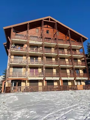 A multi-story building with balconies, a wooden facade, and a ski slope in the foreground. - Facing the slopes, 6-person apartment with terrace (Le Dévoluy)