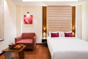 Una habitación de hotel con una cama, un sillón rojo, una mesita con fruta y una obra de arte colgada en la pared.