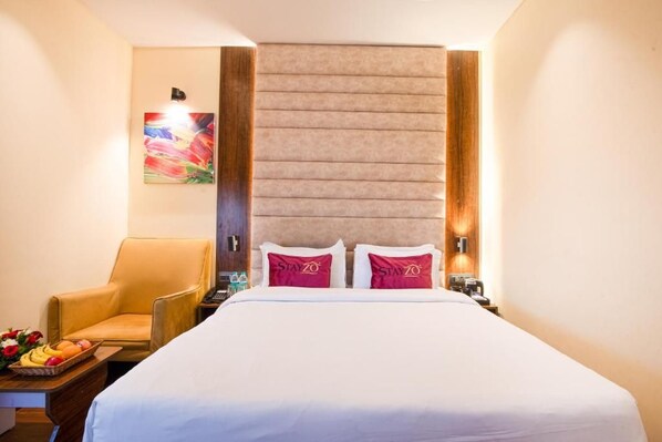 Habitación de hotel con cama, una silla, una mesita de noche y una obra de arte colgada en la pared.