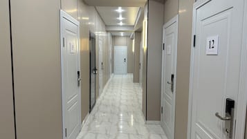 A hotel corridor with numbered doors, a marble floor, and recessed lighting.