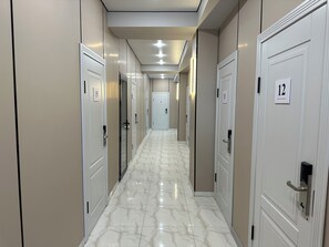 A hotel corridor with numbered doors, a marble floor, and recessed lighting.