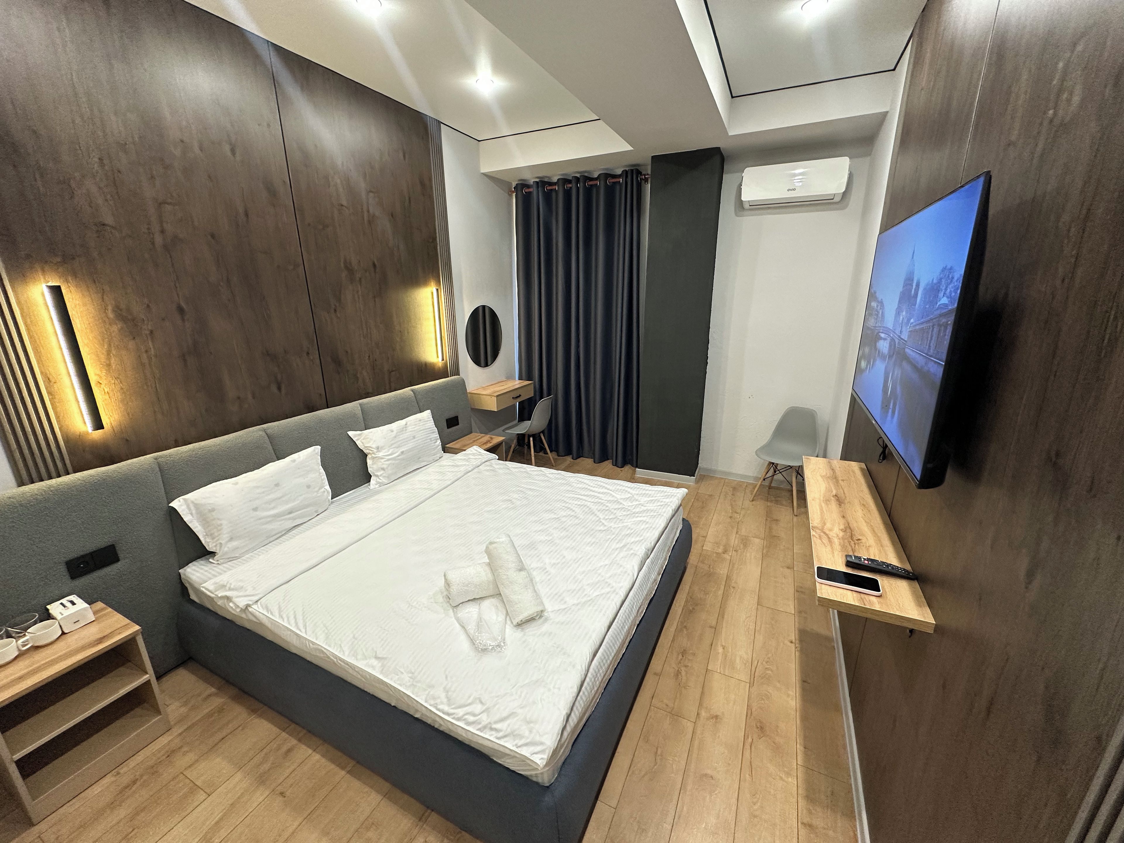 Moderni hotellihuone, jossa on suuri sänky, yöpöydät, työpöytä, tuoli, televisio ja ilmastointilaite.