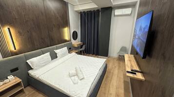 Quarto de hotel moderno com uma cama grande, mesas de cabeceira, escrivaninha, cadeira, televisão e ar condicionado.
