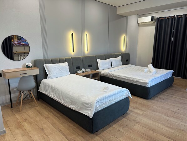 A hotel room with two beds, a desk, a chair, and a mirror.