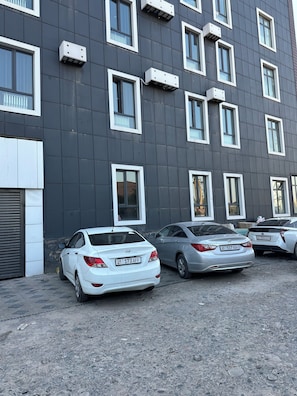 A building with multiple windows and a parking area with cars. - Gatsby Lva Tolstogo (Bishkek)