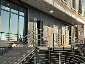 A building with a metal staircase leading to a balcony, large windows, and a door.