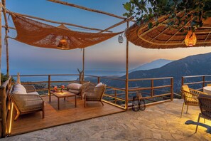 Une terrasse en bois avec des meubles en osier, une table et un luminaire suspendu.