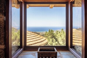 Une pièce dotée d’une grande fenêtre donnant sur un paysage de champs en terrasses et offrant une vue sur la mer.