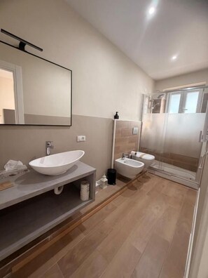 A modern bathroom with a large mirror, two sinks, a shower enclosure, and a wooden floor. - Franciacorta White (Cellatica)