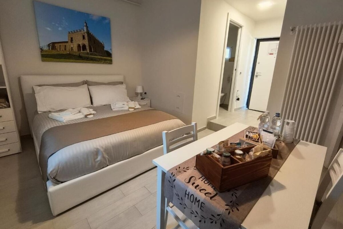 A hotel room with a bed, a dining table with a tray of items, a painting on the wall, and a view into the bathroom.