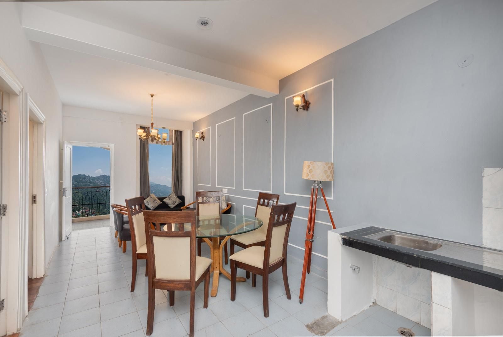 A dining area with a glass table and wooden chairs, a floor lamp, and a view of the outdoors.