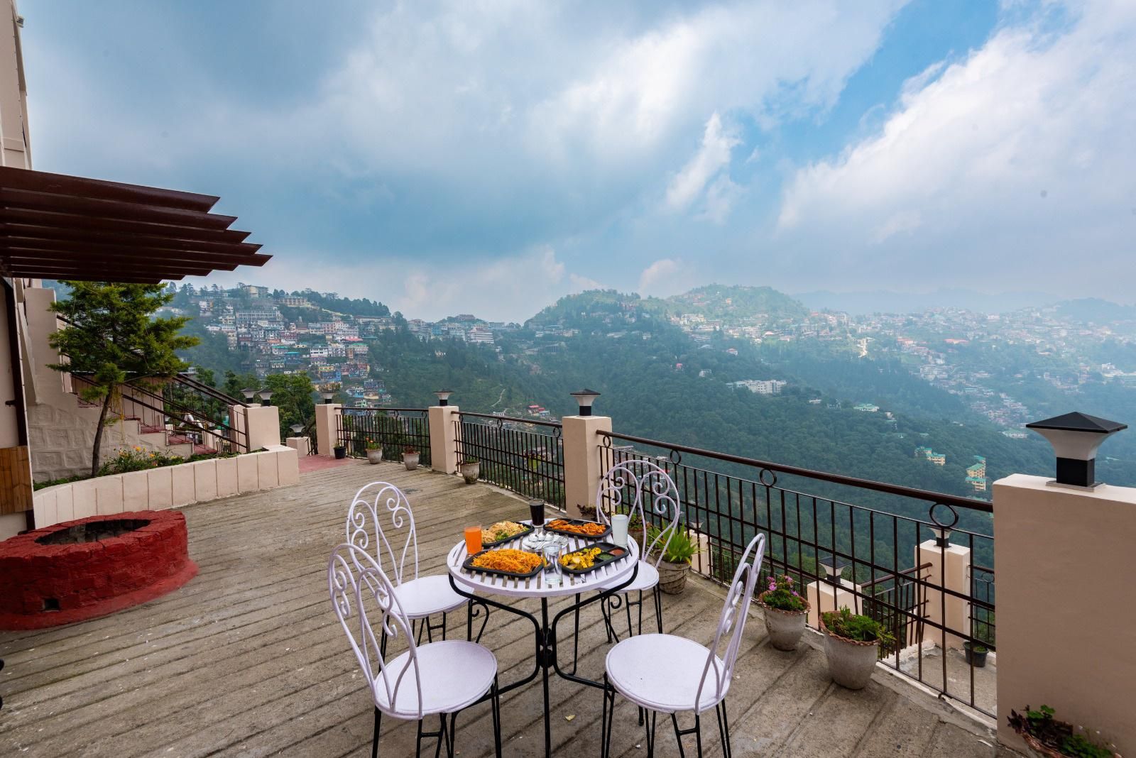 A terrace with a table set for dining, overlooking a mountainous landscape.