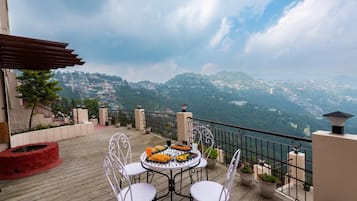 A terrace with a table set for dining, overlooking a mountainous landscape.