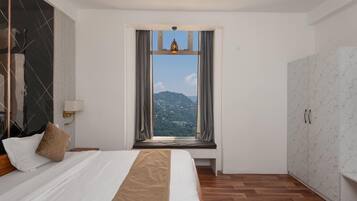 A hotel room with a bed, a window with curtains, a view of a mountainous landscape, and a wardrobe.