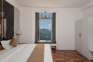 Quarto de hotel com cama, janela com cortinas, vista para uma paisagem montanhosa e guarda-roupa.
