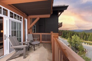 A wooden balcony with two chairs and a table, overlooking a forested area with mountains in the distance. - Peakside at One Ski Hill: Peak 8 Ski-In/Out, 2 Baths, A/C, Pools, Shuttle (Breckenridge)