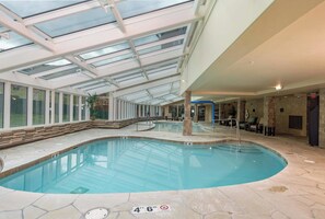 An indoor swimming pool with a glass ceiling, stone flooring, and a lounge area with chairs and a table. - Peakside at One Ski Hill: Peak 8 Ski-In/Out, 2 Baths, A/C, Pools, Shuttle (Breckenridge)