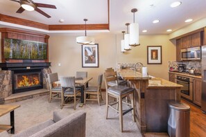 A modern kitchen with a central island, a dining area with chairs, a fireplace, and a ceiling fan. - Peakside at One Ski Hill: Peak 8 Ski-In/Out, 2 Baths, A/C, Pools, Shuttle (Breckenridge)