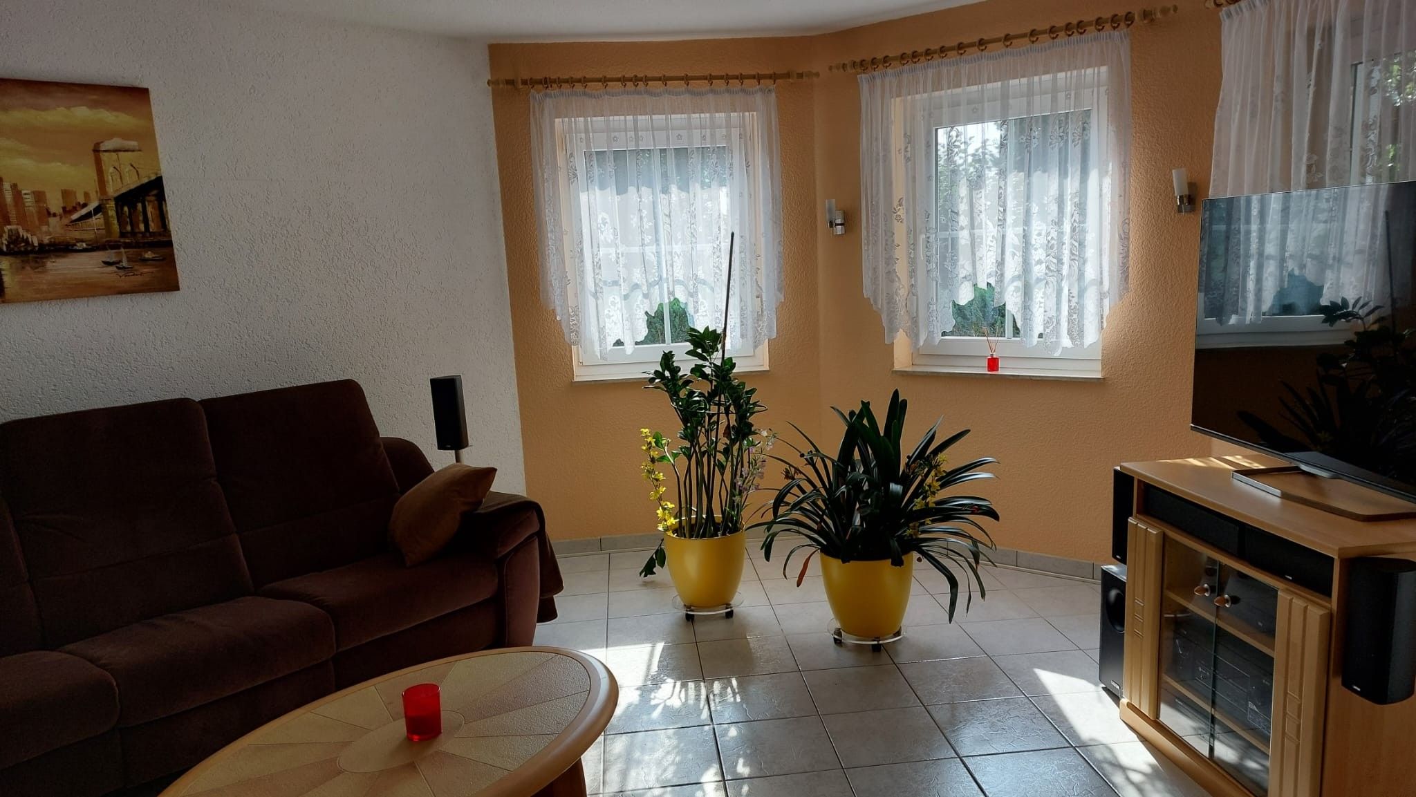 Ein Wohnzimmer mit einem braunen Sofa, zwei gelben Blumentöpfen, einem Fernseher und einem Gemälde an der Wand.