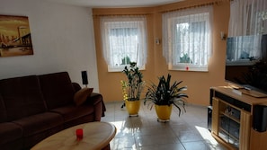 Ein Wohnzimmer mit einem braunen Sofa, zwei gelben Blumentöpfen, einem Fernseher und einem Gemälde an der Wand.