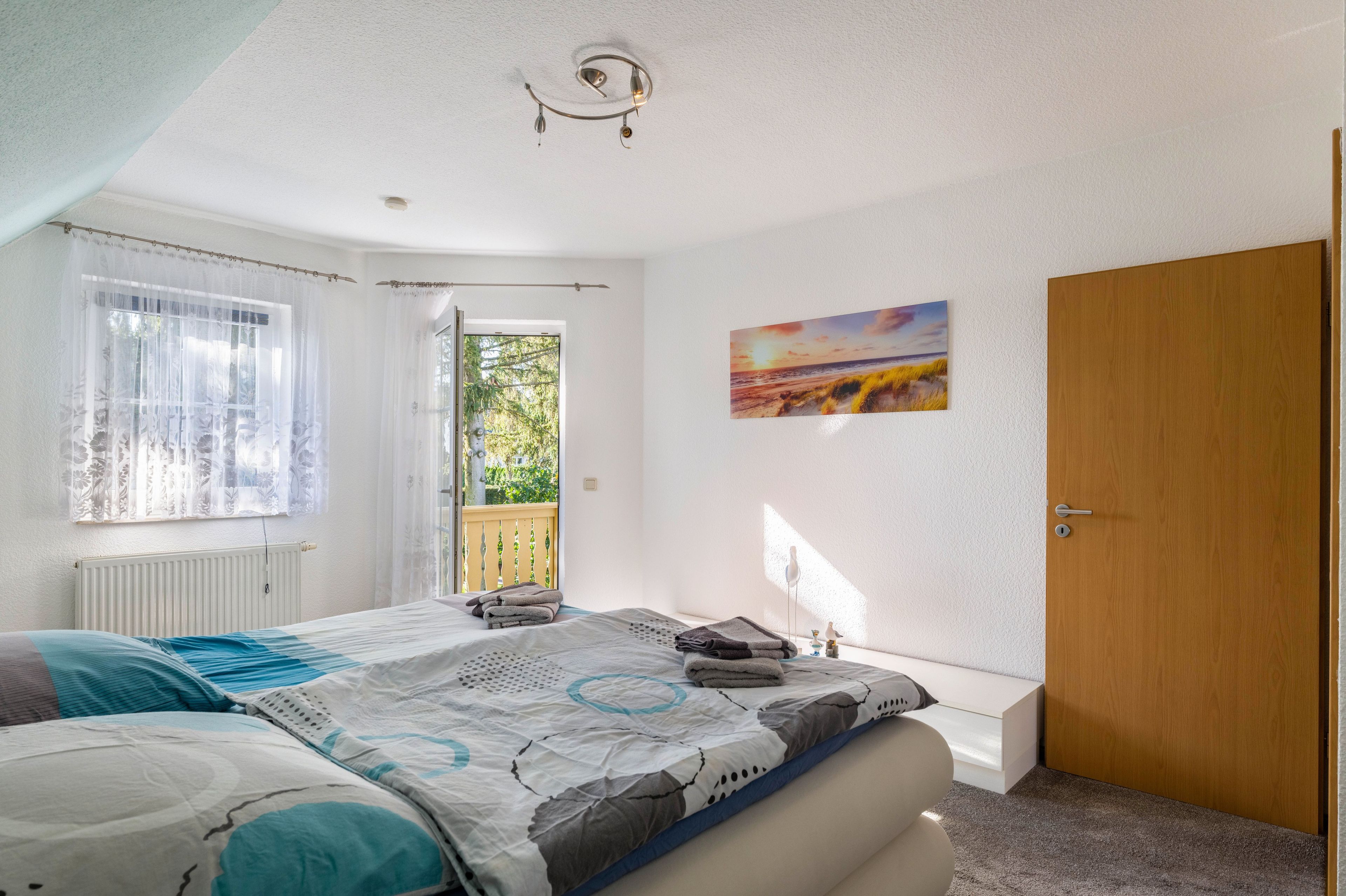 A bedroom with a bed, a window with curtains, a door, and a painting on the wall.