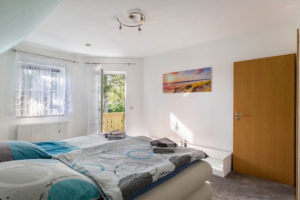 A bedroom with a bed, a window with curtains, a door, and a painting on the wall.