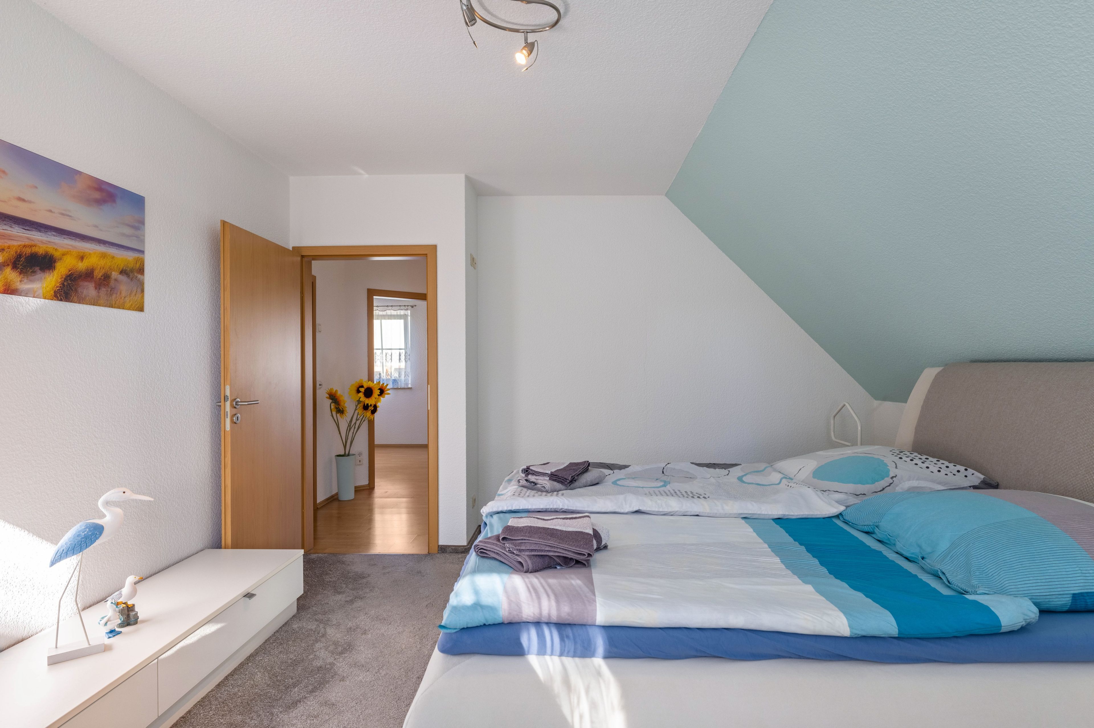 A bedroom with a bed, a bedside table, a dresser, a painting, and a vase with sunflowers.