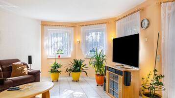 A living room with a sofa, a coffee table, a TV, and potted plants.
