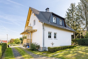 A two-story house with a sloped roof, a balcony, and a well-maintained garden.