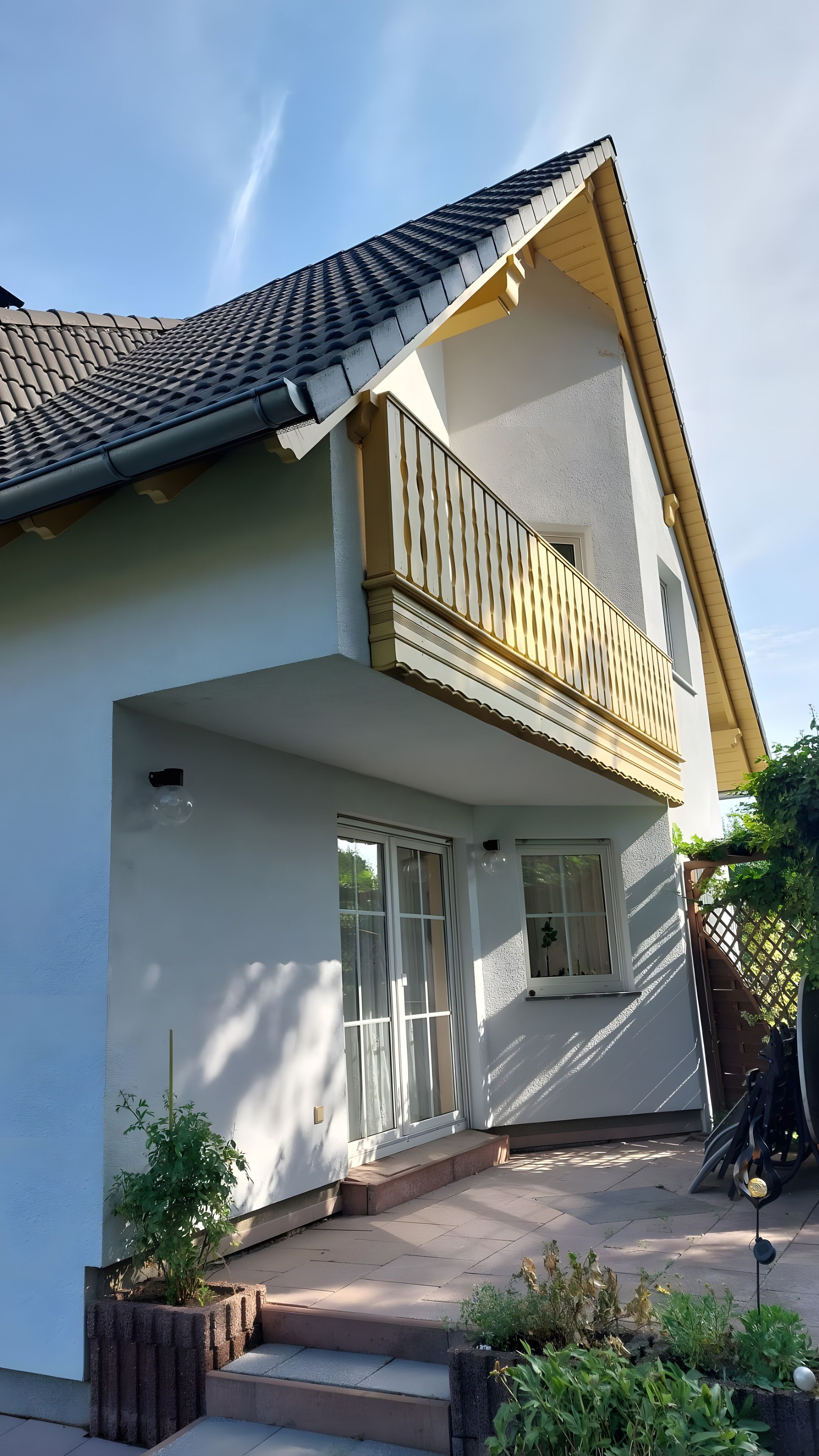 A two-story house with a balcony, large windows, and a tiled roof.