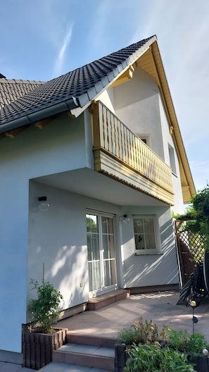 Ein zweistöckiges Haus mit Balkon, großen Fenstern und einem Ziegeldach.