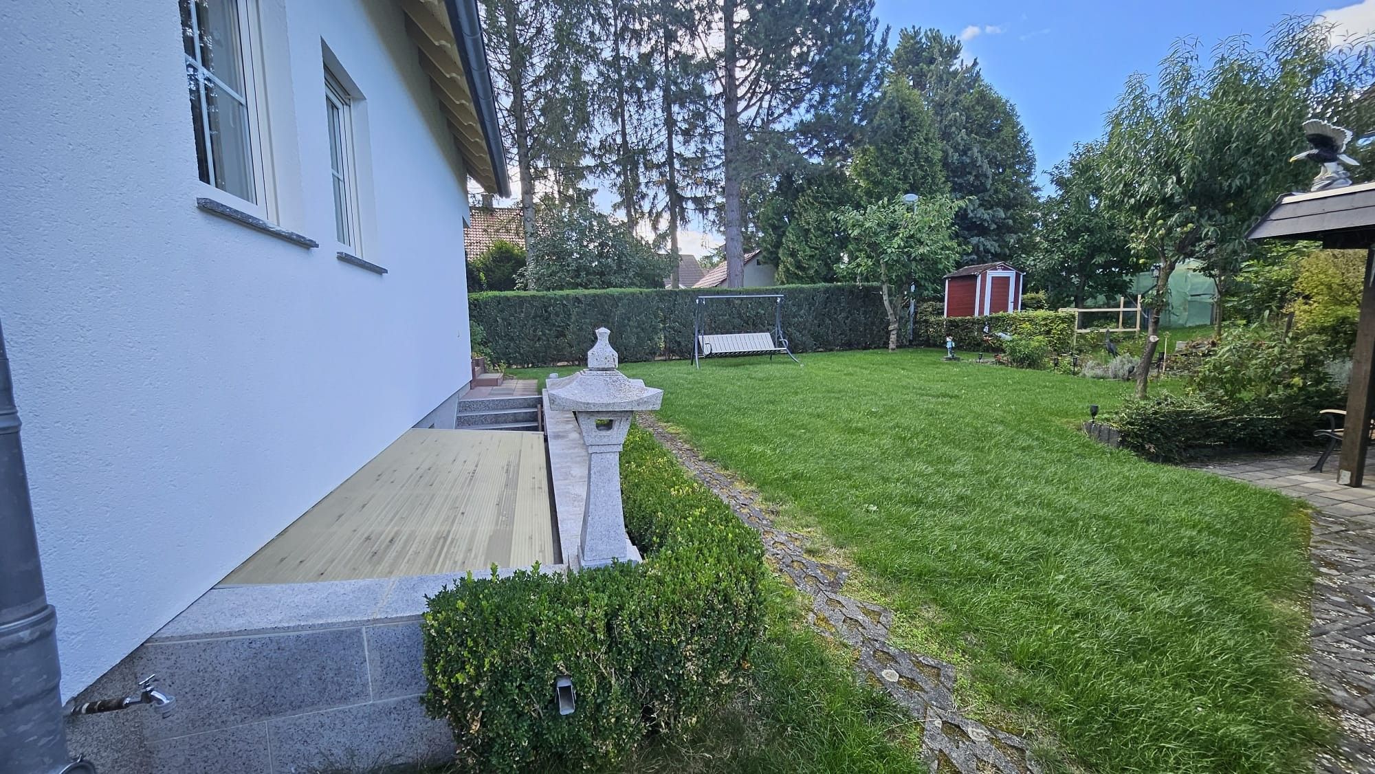 A well-maintained garden with a paved pathway, a stone lantern, and a small statue.