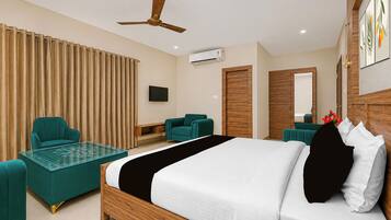 Habitación de hotel con cama, dos sillones, televisor, aire acondicionado y ventilador de techo.