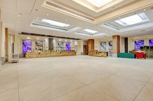 Um hall amplo com teto alto, iluminação embutida e um balcão de recepção com um painel decorativo.
