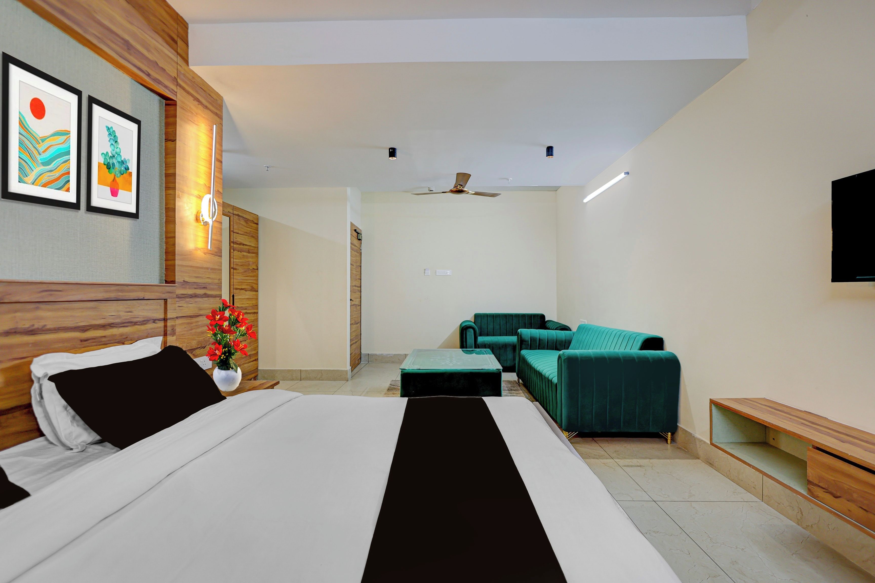 A modern hotel room with a bed, a sofa, a TV, and artwork on the wall.