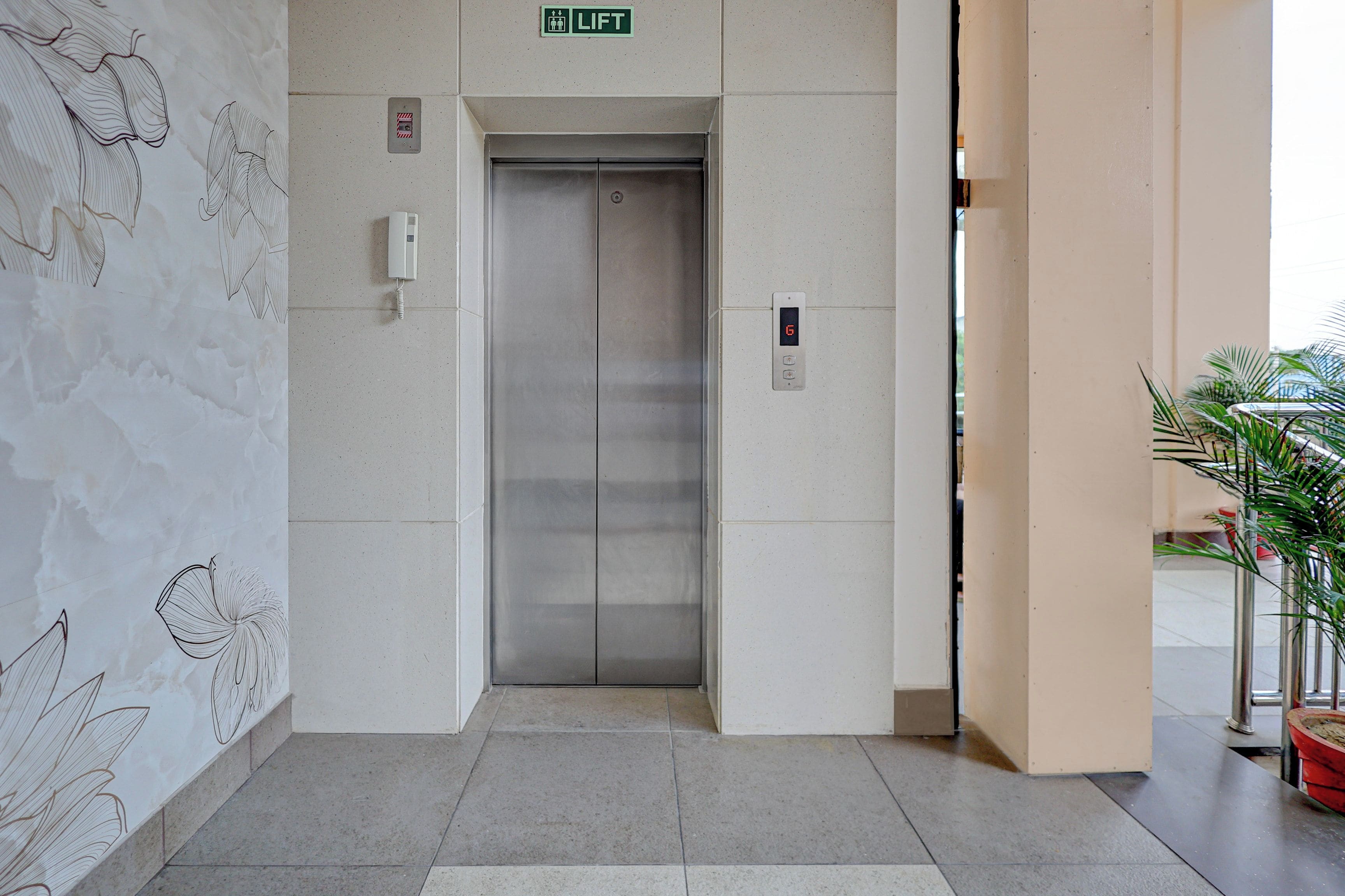 An elevator with a digital display, a lift sign above, and a wall with abstract line drawings.